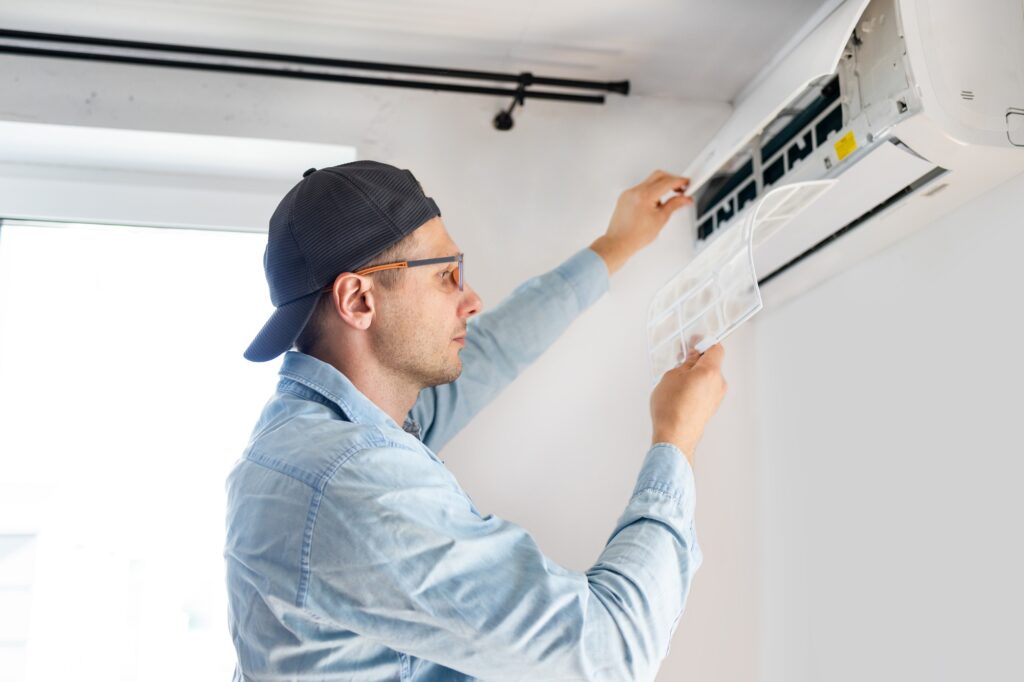 Young male technician repairing air conditioner indoors.